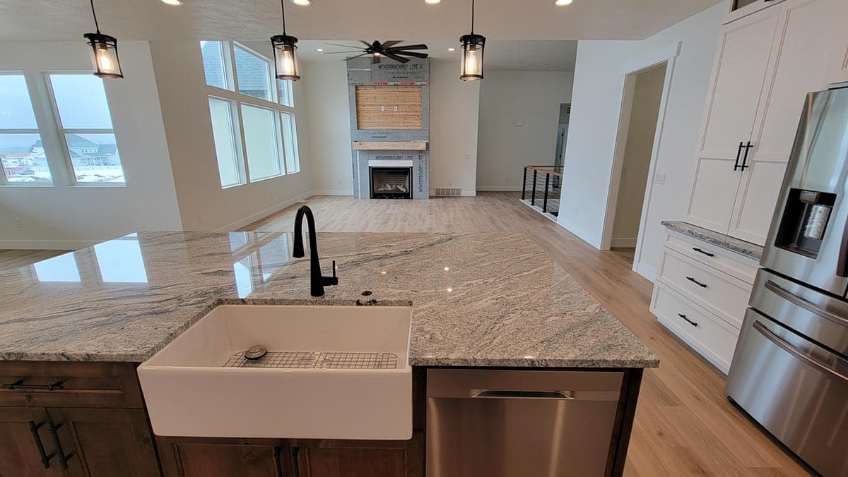 Open concept interior: kitchen island with farmhouse sink, living area with fireplace, and staircase with railing.