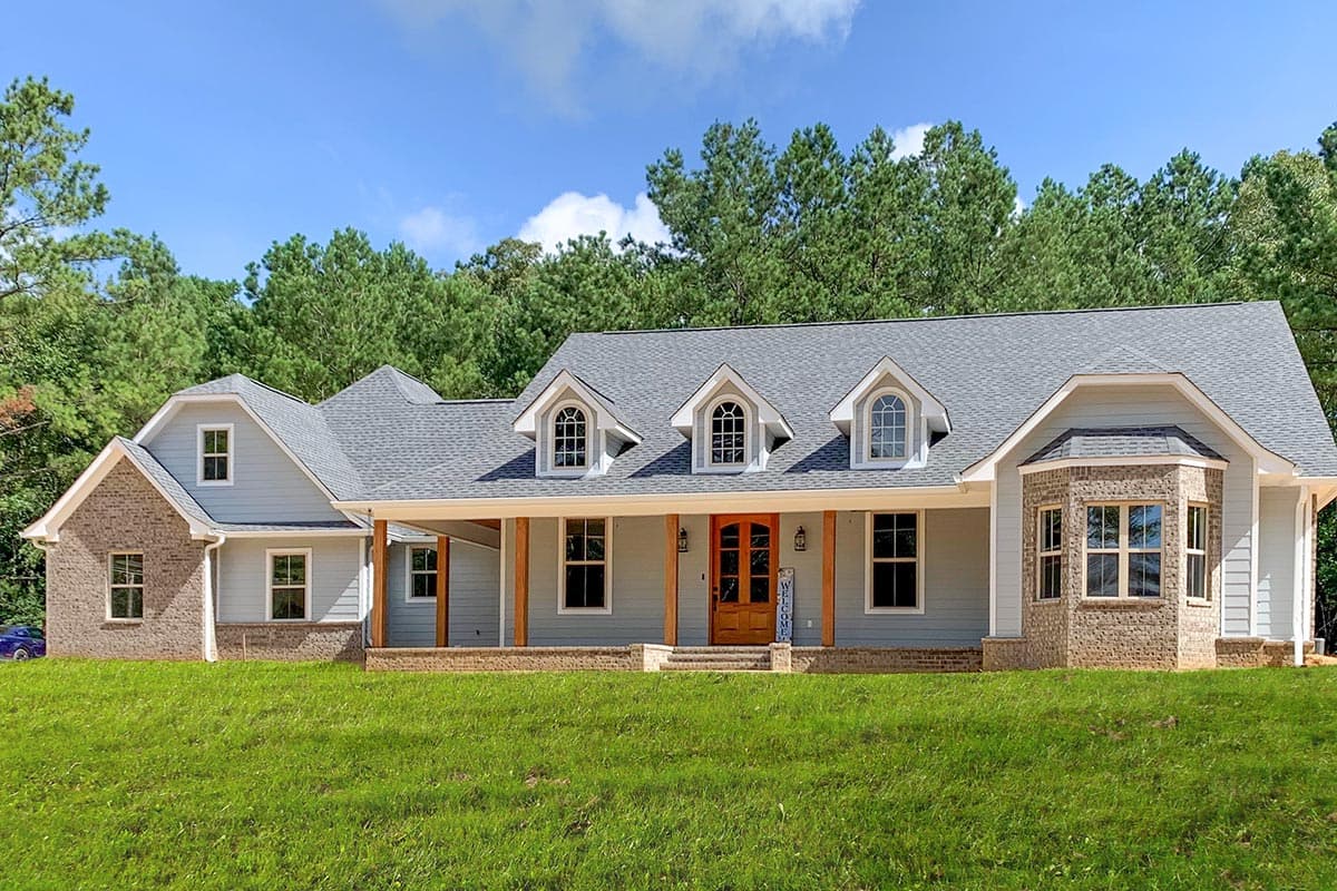 House plan exterior with Craftsman-style elements. Features include dormers, a covered porch with wood columns, and a brick accent wall. Single story.