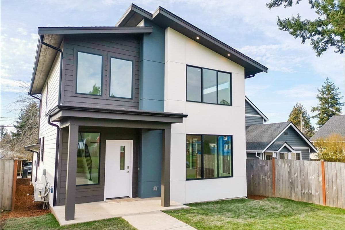 Modern house plan exterior with two stories. Features a covered entry, dark trim around large windows, and a combination of siding materials.