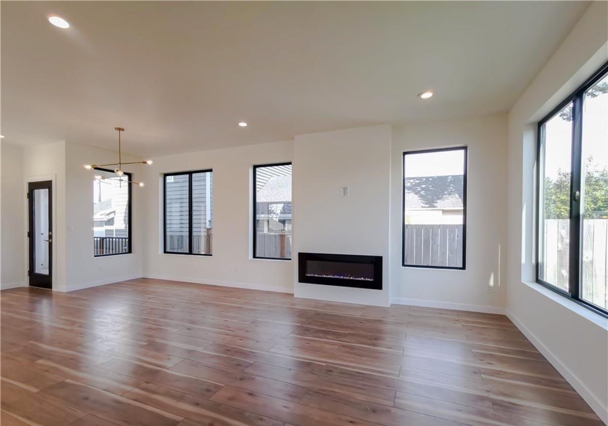 Interior view of open living space with fireplace, large windows, and wood flooring.