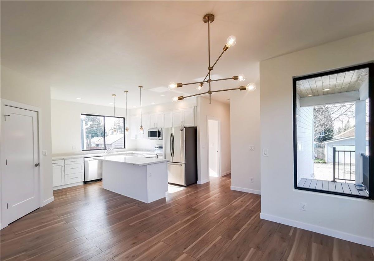 Open concept kitchen with white island and cabinets, stainless steel appliances, and modern chandelier.
