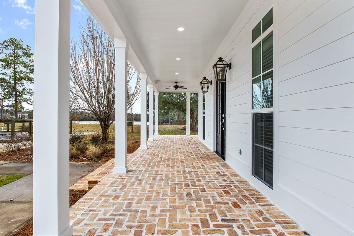 House plan exterior featuring a wide covered porch with brick pavers, white columns, and gas lanterns.