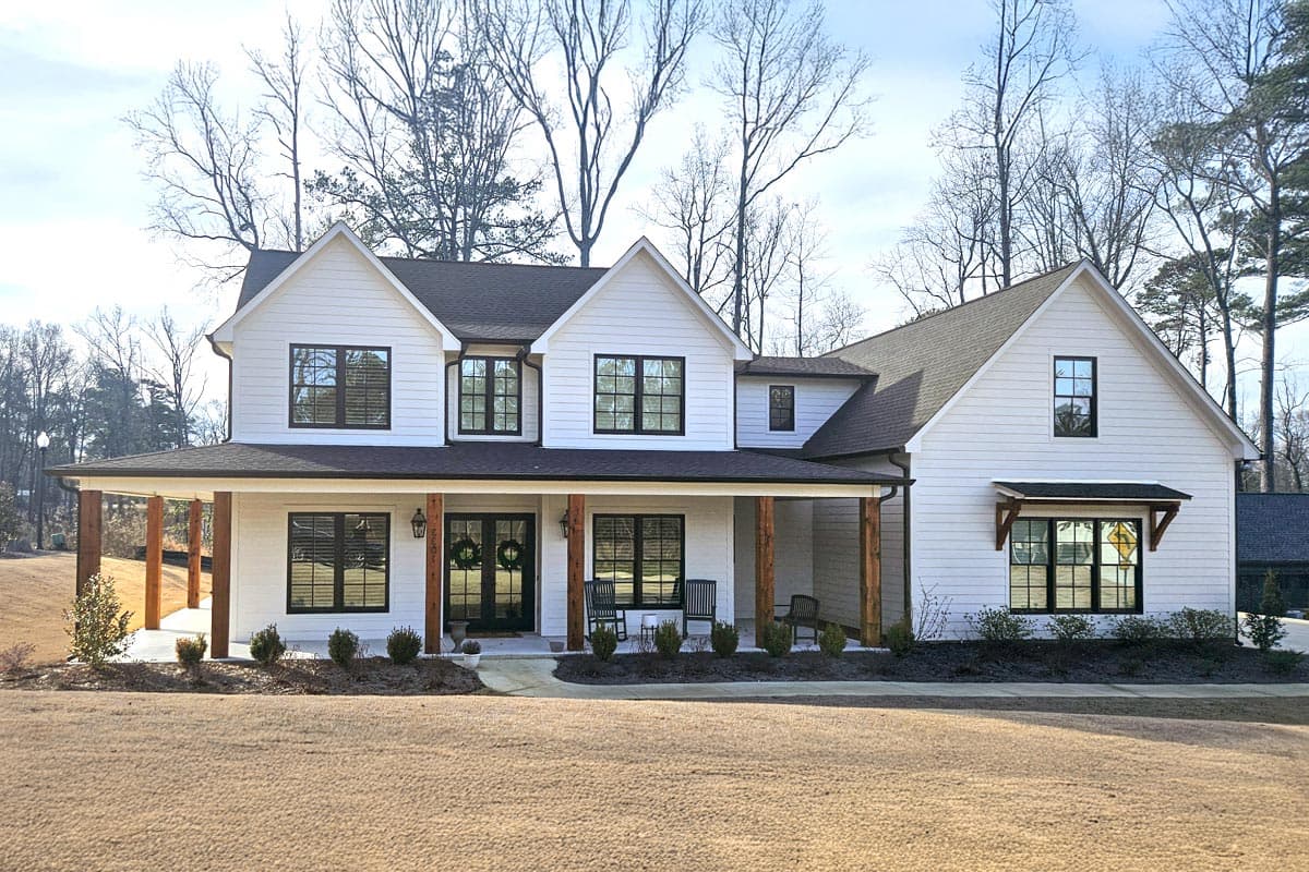 House plan exterior. Two-story Modern Farmhouse with a gabled roof, prominent front porch with wood columns, and multiple dormers.