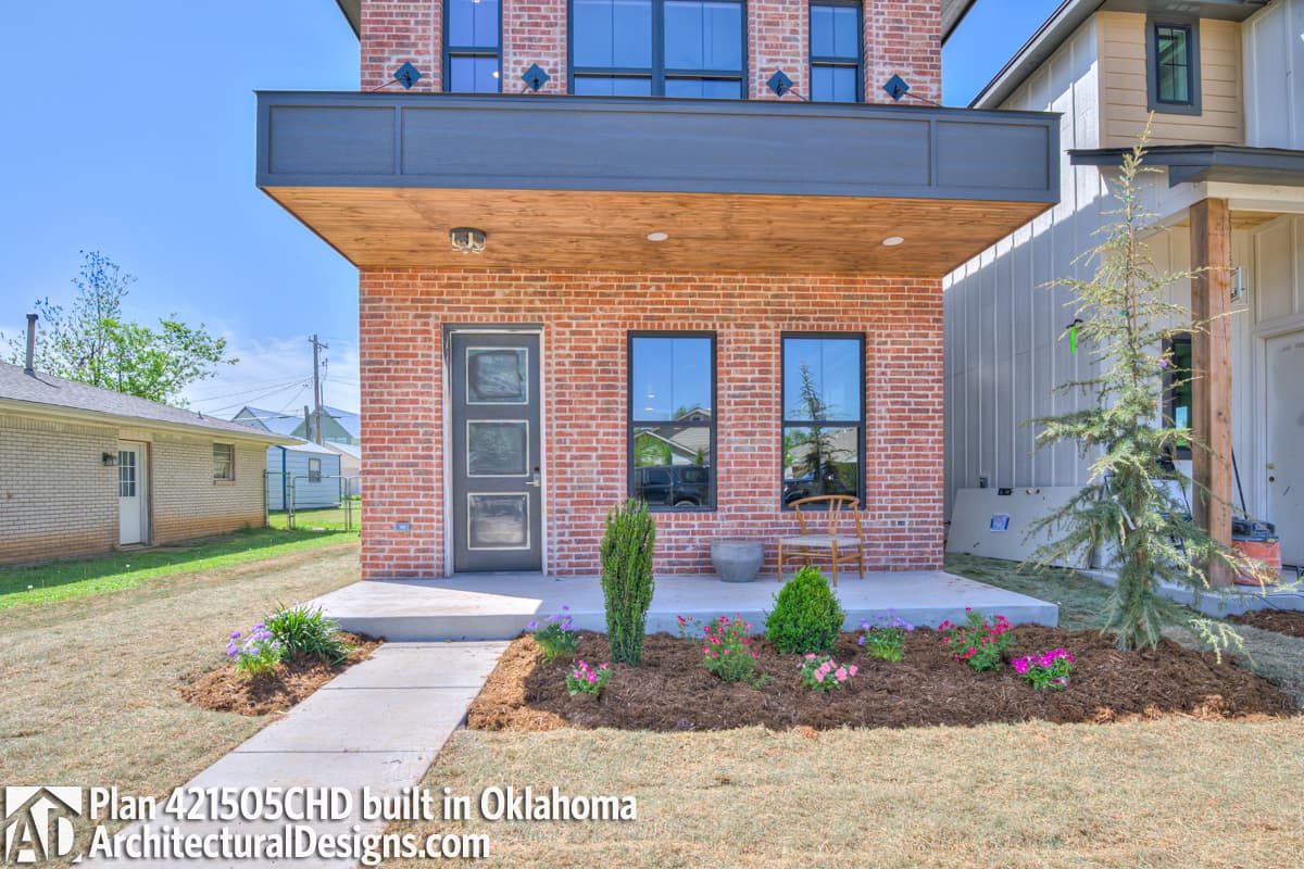 House plan exterior with red brick facade, second-story cantilever, and covered porch. Plan 421505CHD.
