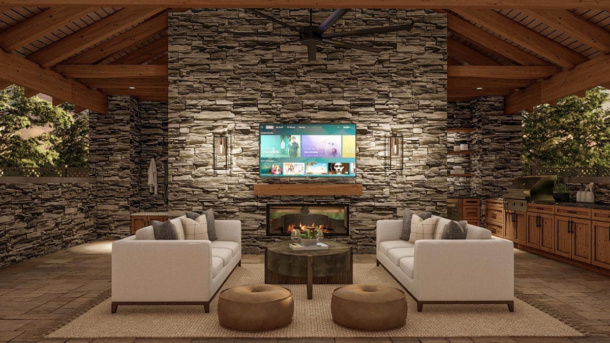 Cozy outdoor living space featuring a stone fireplace with TV, seating, and a nearby grill. Wooden beams and a stone wall add warmth to the area.