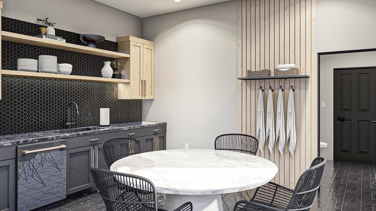 Modern interior with a round white marble table surrounded by black chairs. A kitchenette and door with hanging towels are visible.