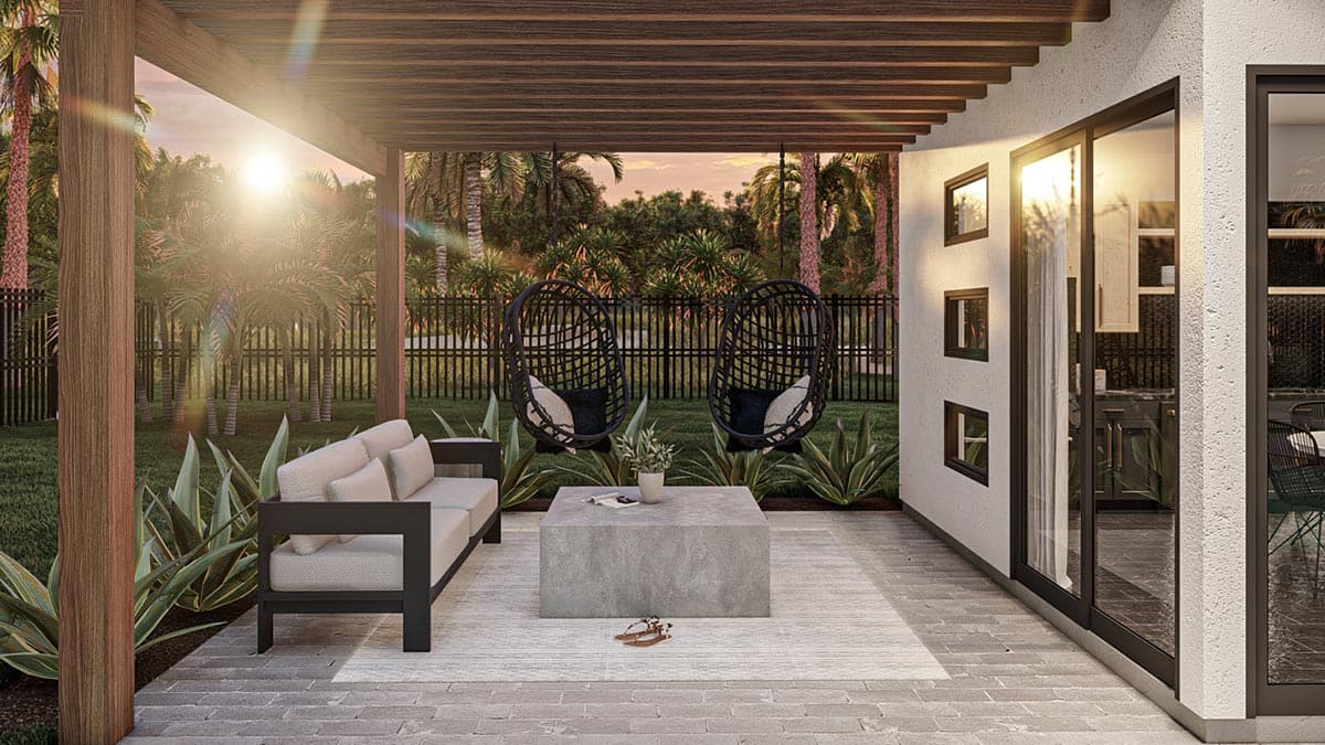 A modern outdoor patio with a sofa, concrete coffee table, and hanging chairs overlooking a lawn and tropical landscape at sunset.