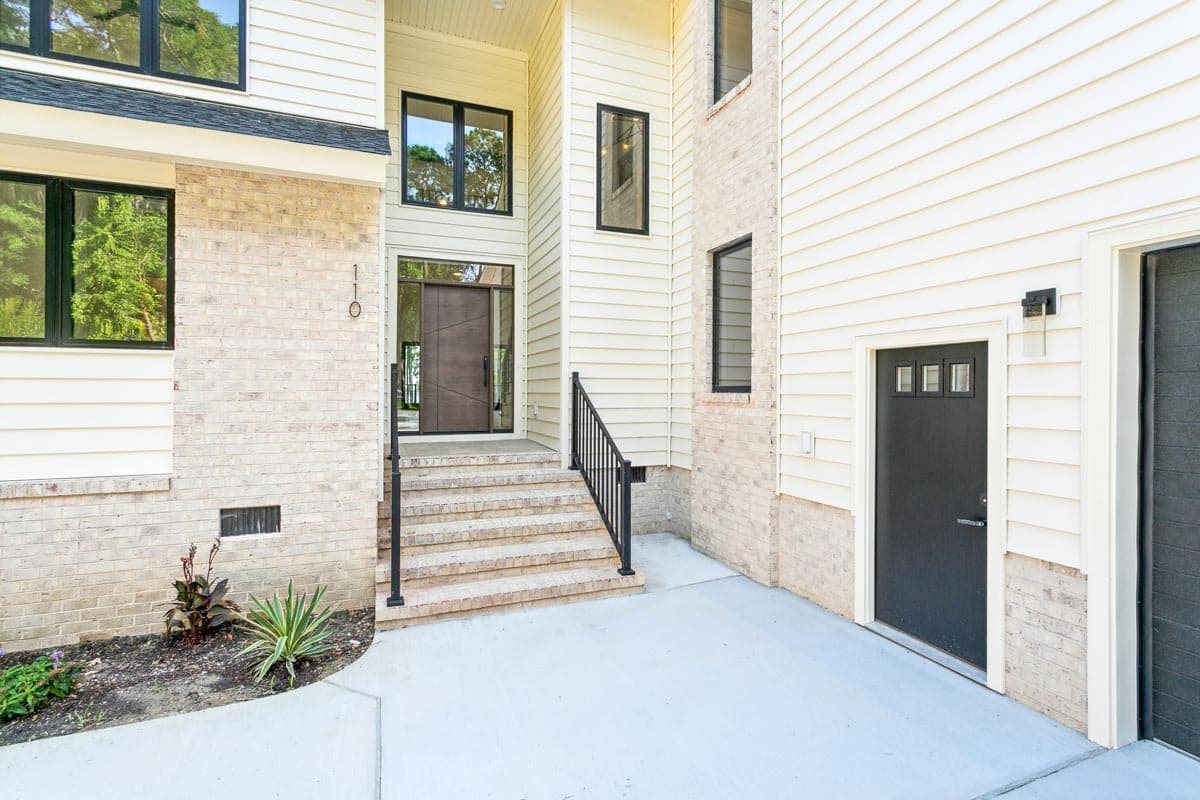 House plan exterior with beige brick base, siding, a modern wood door, and black-framed windows.
