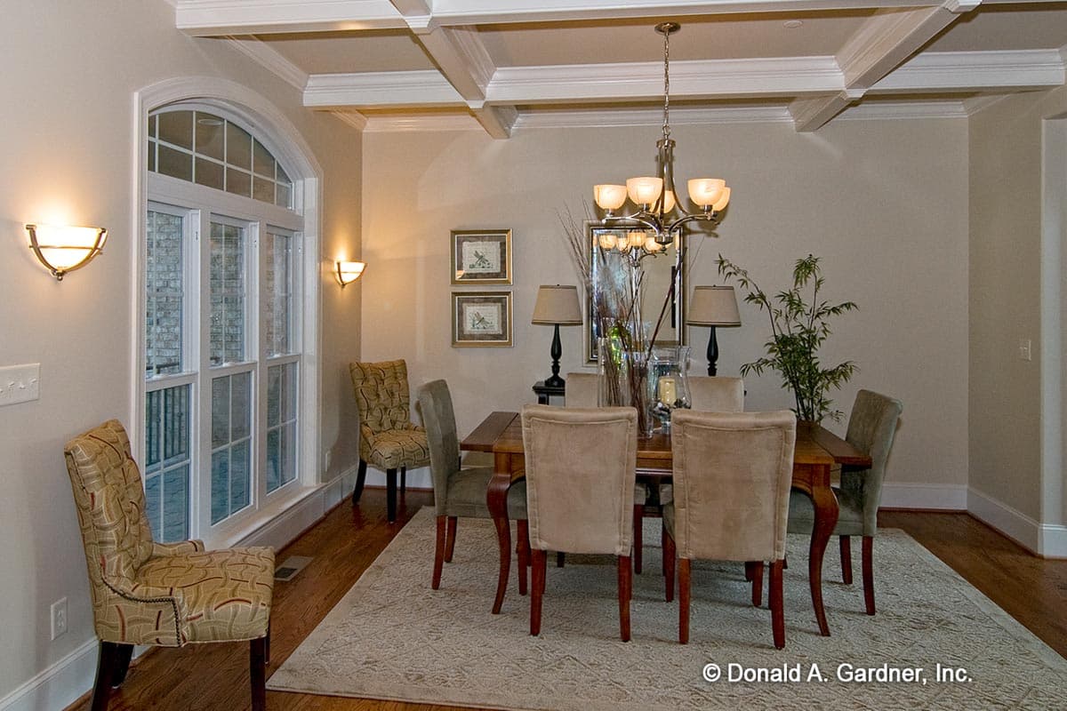 Dining room with coffered ceiling, large arched window, and a wooden table with upholstered chairs.