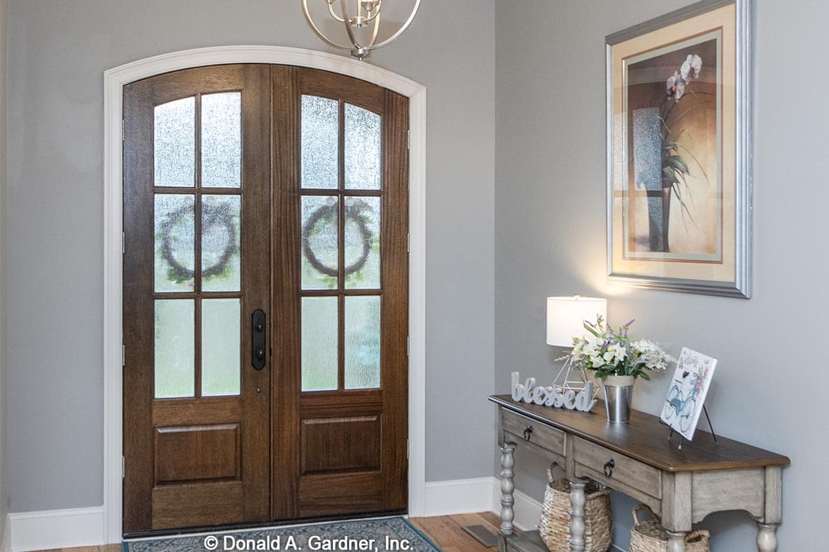 Double wooden arched entry doors with glass panes and trim, flanking a console table with decor.