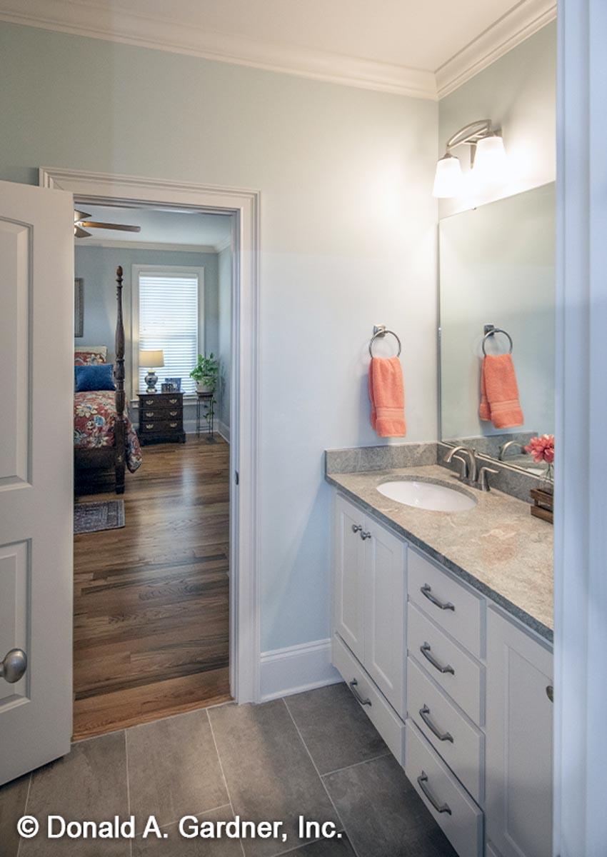 Bathroom vanity with single sink and granite countertop, doorway opens to bedroom with four-poster bed.