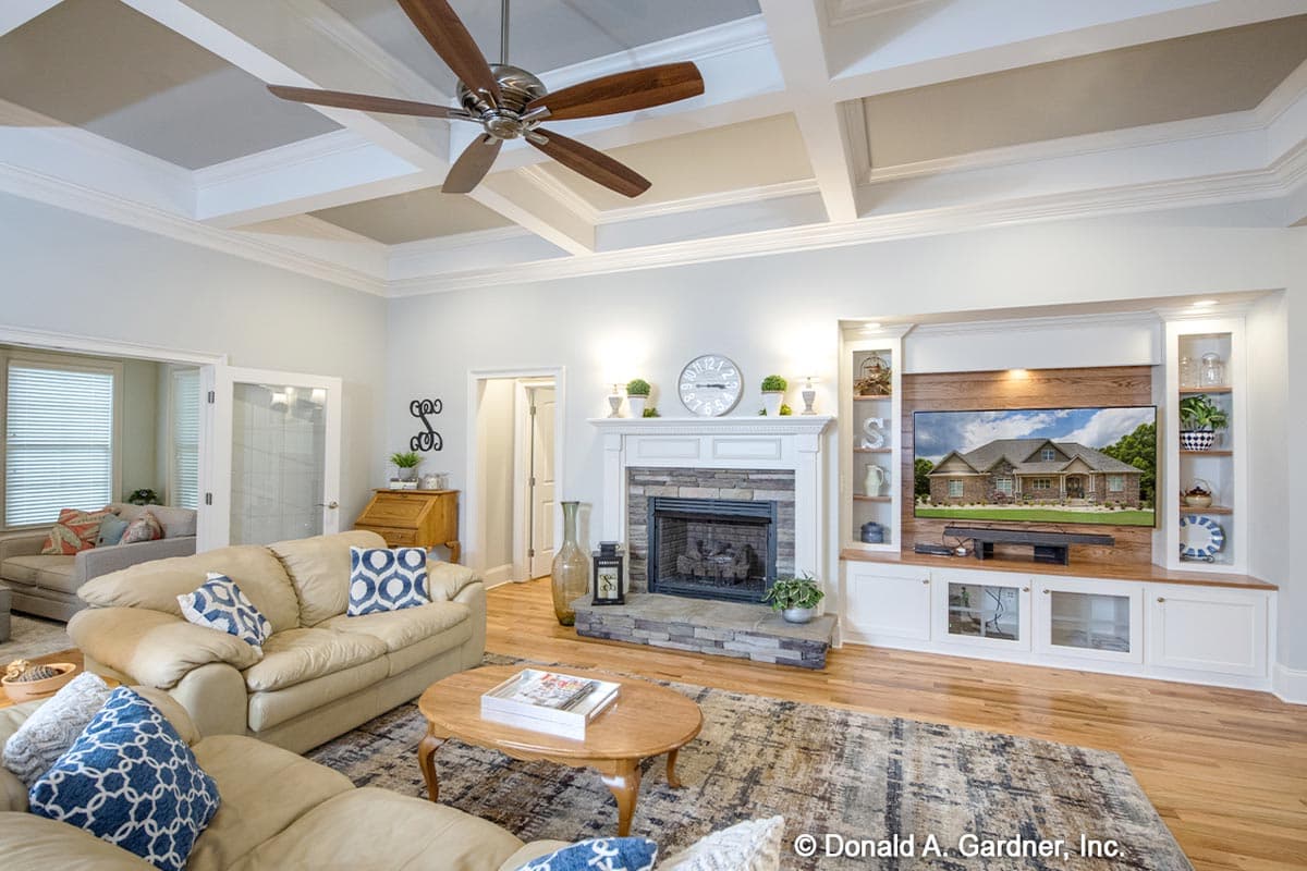 Great room with coffered ceiling, stone fireplace, built-in entertainment center, and wood floors.