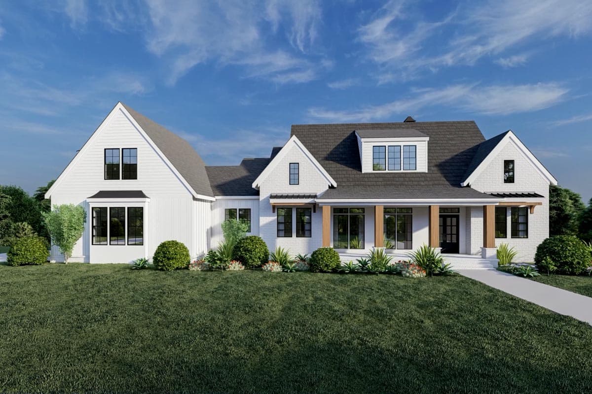 A modern, white farmhouse with a gray roof and black window frames sits on a well-manicured lawn under a blue, cloudy sky.