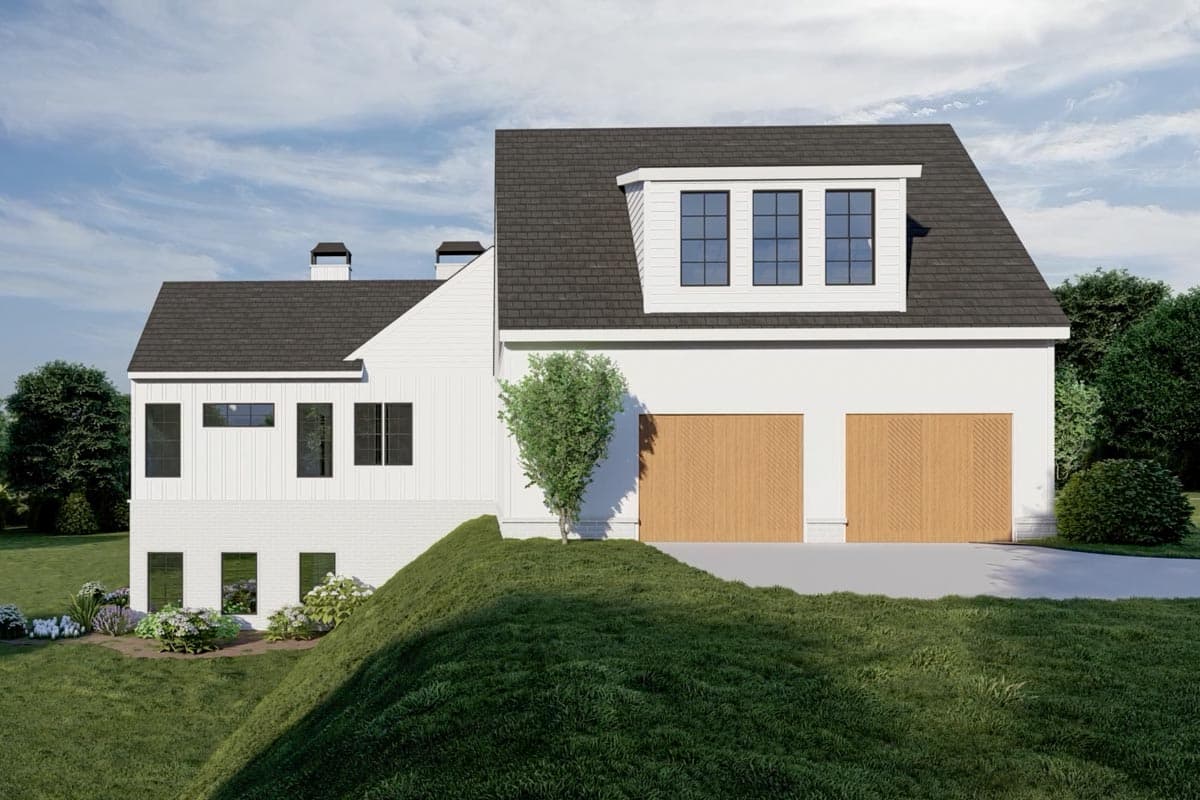 A modern, white house with a dark roof and wooden garage doors. It is situated on a hill with green grass and small shrubs in front.