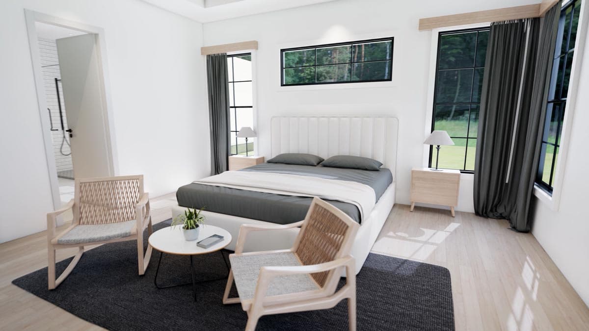 A modern bedroom with a large bed, two wicker chairs, and a small table. Large windows provide natural light and views of green trees outside.