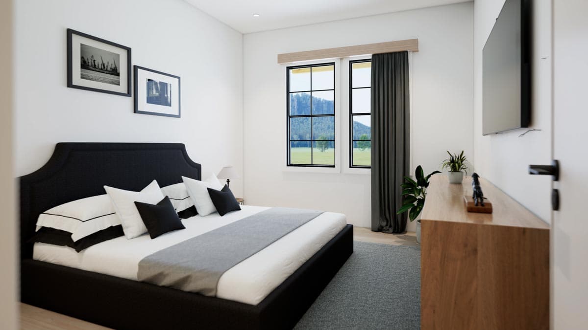 A modern bedroom features a black bed with white and black pillows, framed art, and a large window with a view of a lush landscape.