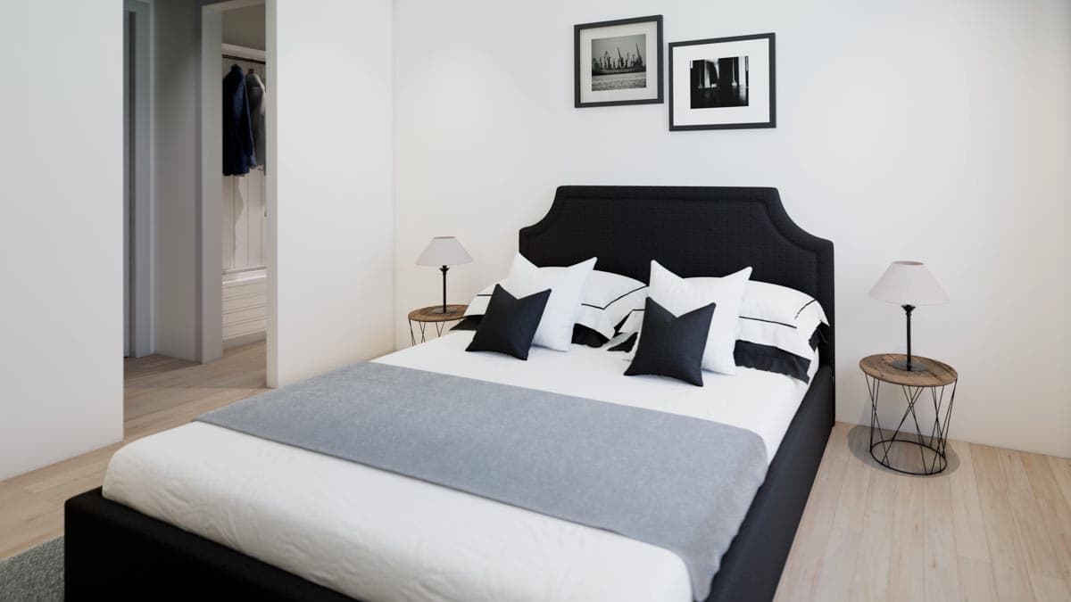 A modern bedroom with a black headboard, white bedding, and grey throw. Two black pillows accent the white pillows, with framed art above.