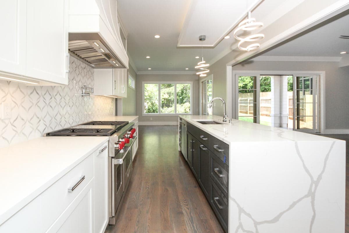 Modern kitchen featuring a large island with sink, professional range, white cabinetry, and tile backsplash, open to dining area.