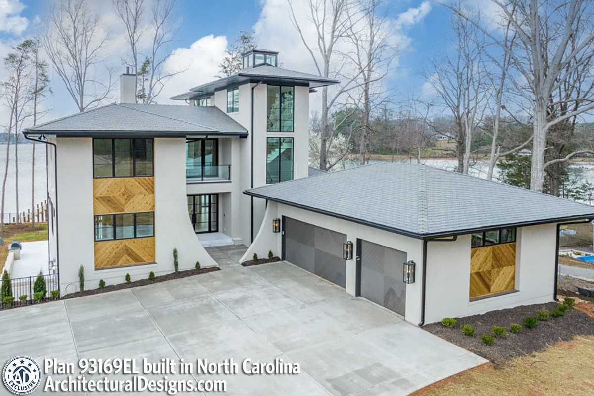 Modern house plan exterior with a three-story tower, flat roofs, large windows, and a detached three-car garage.