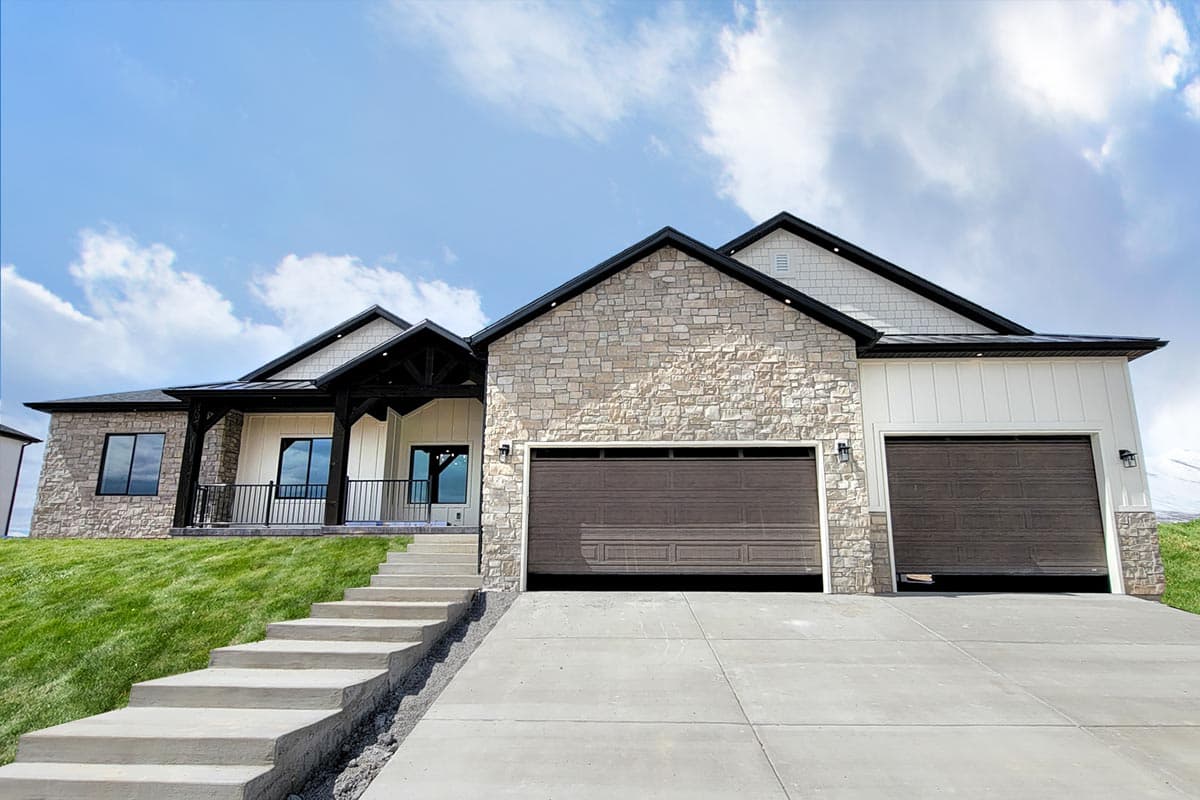 House plan exterior with stone veneer, two-car garage, and a covered porch. Gable roofline with black trim and dark garage doors.