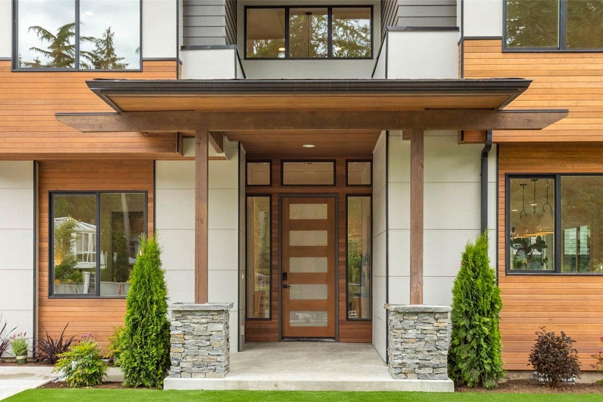 Modern house plan exterior with wood siding, stone pillars, cantilevered roof, and multi-pane entry door.