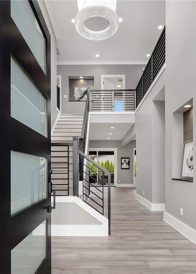 Interior view of modern foyer with open-riser staircase, black metal railings, and minimalist art.