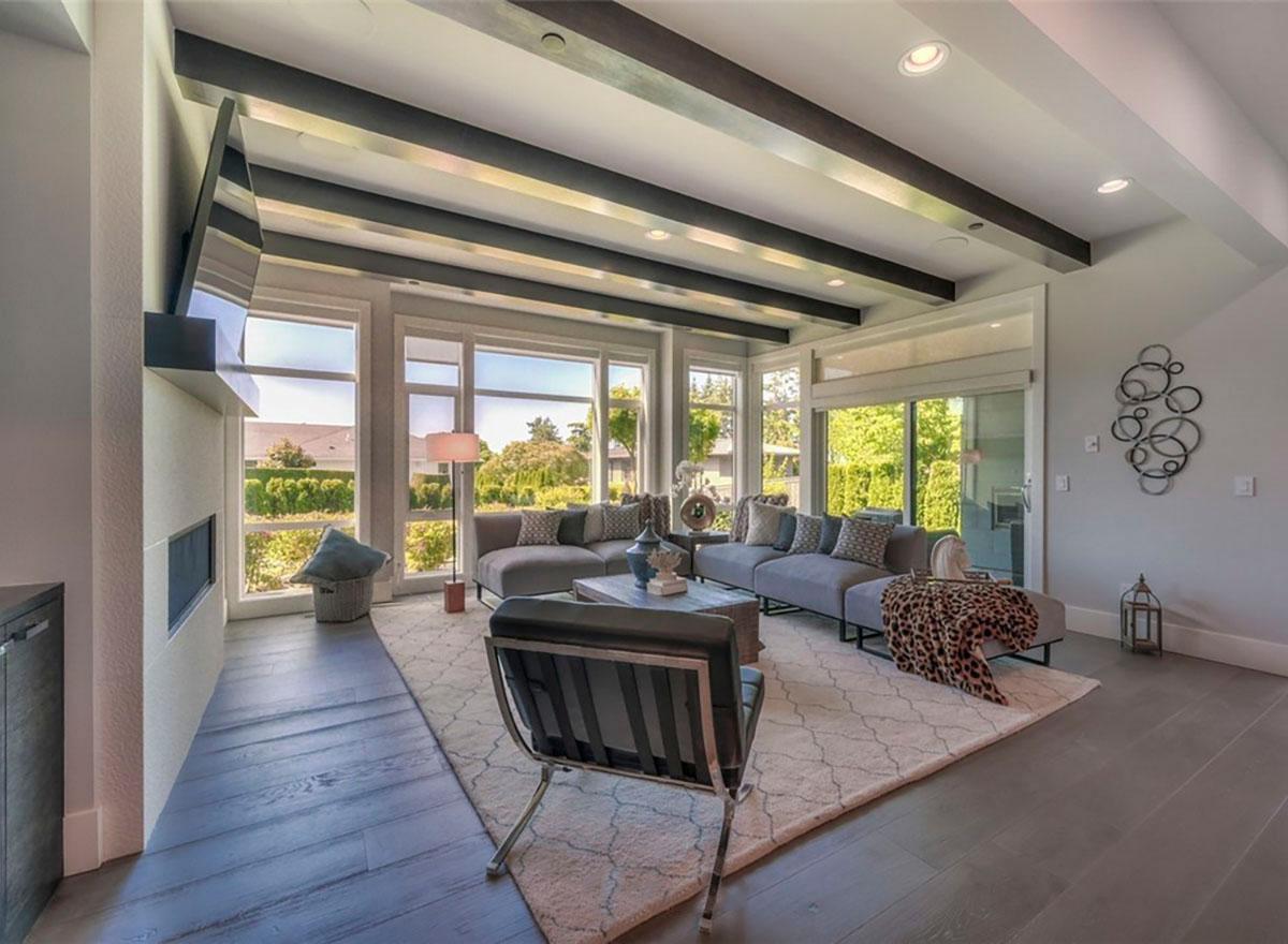 Contemporary living room with sectional sofa, fireplace, large windows, and exposed dark wood ceiling beams.
