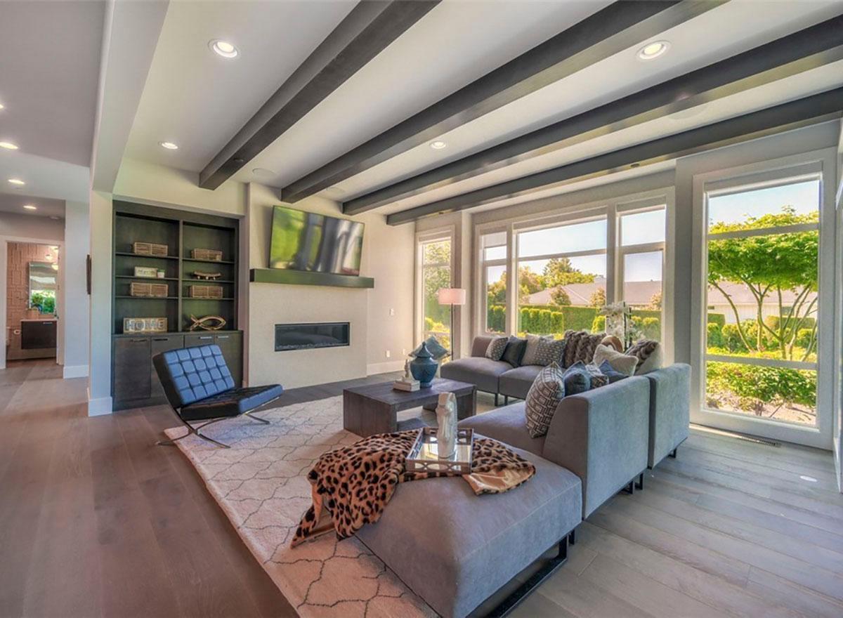 Living room with fireplace, built-in shelving, large windows, and exposed ceiling beams.