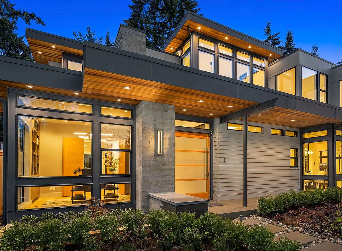 Modern house exterior with cantilevered rooflines, extensive glass windows, and natural wood accents.