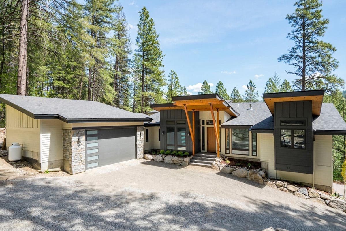 House plan exterior. Modern style, single story. Features include an open porch with wood supports, shed rooflines, and stone accents.