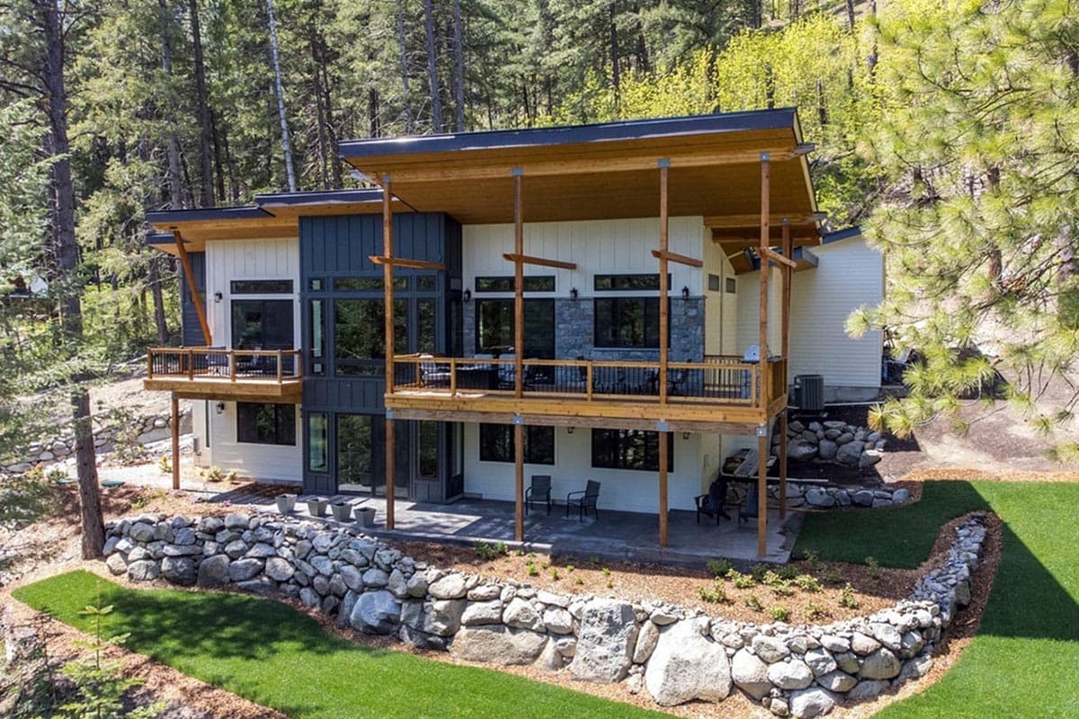 Modern house plan exterior with multiple decks, large windows, stone accents, and sloped rooflines.