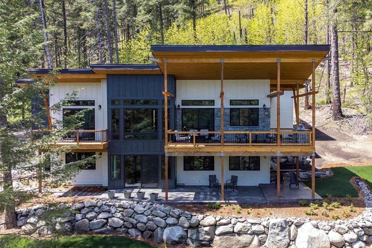 Modern house plan exterior with overlapping rooflines, extensive windows, balconies, and wood and stone accents.