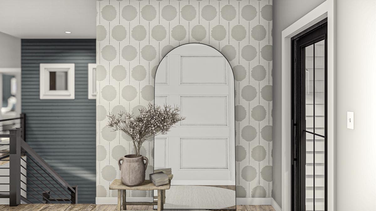 Interior view of entryway with patterned wallpaper, arched mirror reflecting a paneled door, and a staircase.