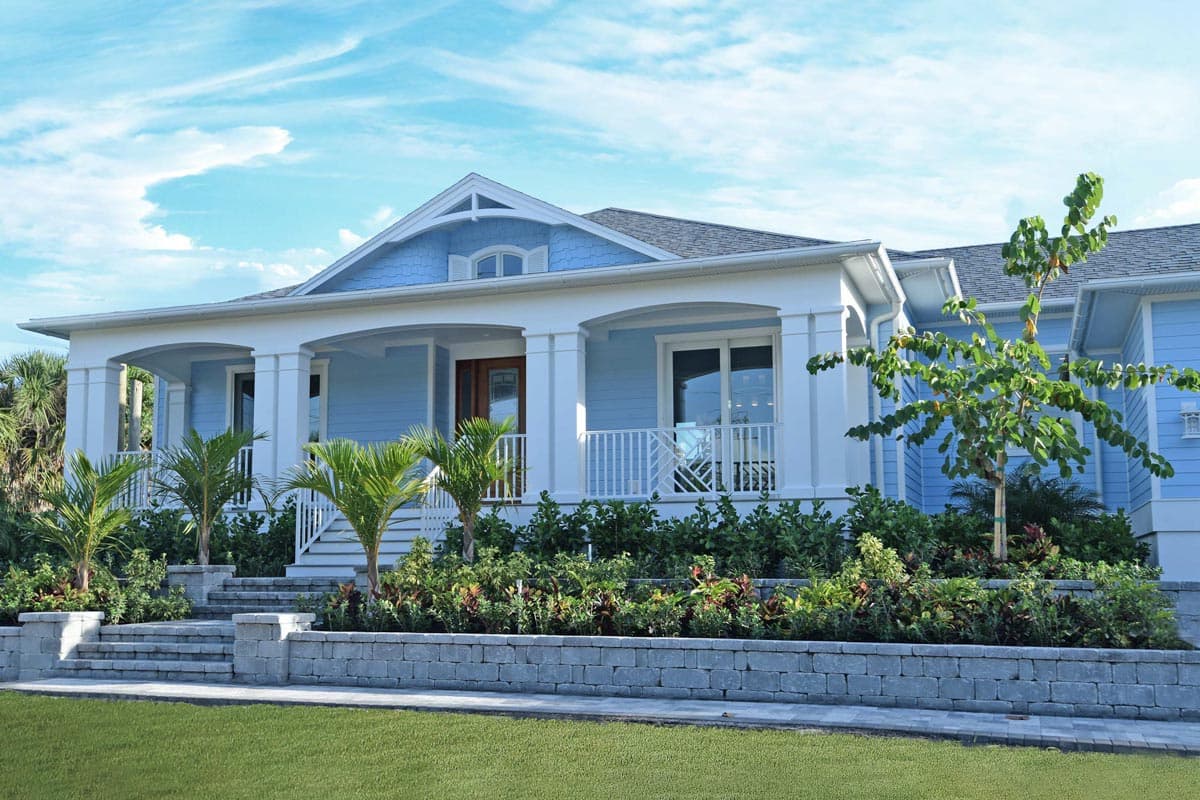 House plan exterior featuring a one-story Modern Coastal home with a wraparound porch, prominent gables, and decorative dormer.