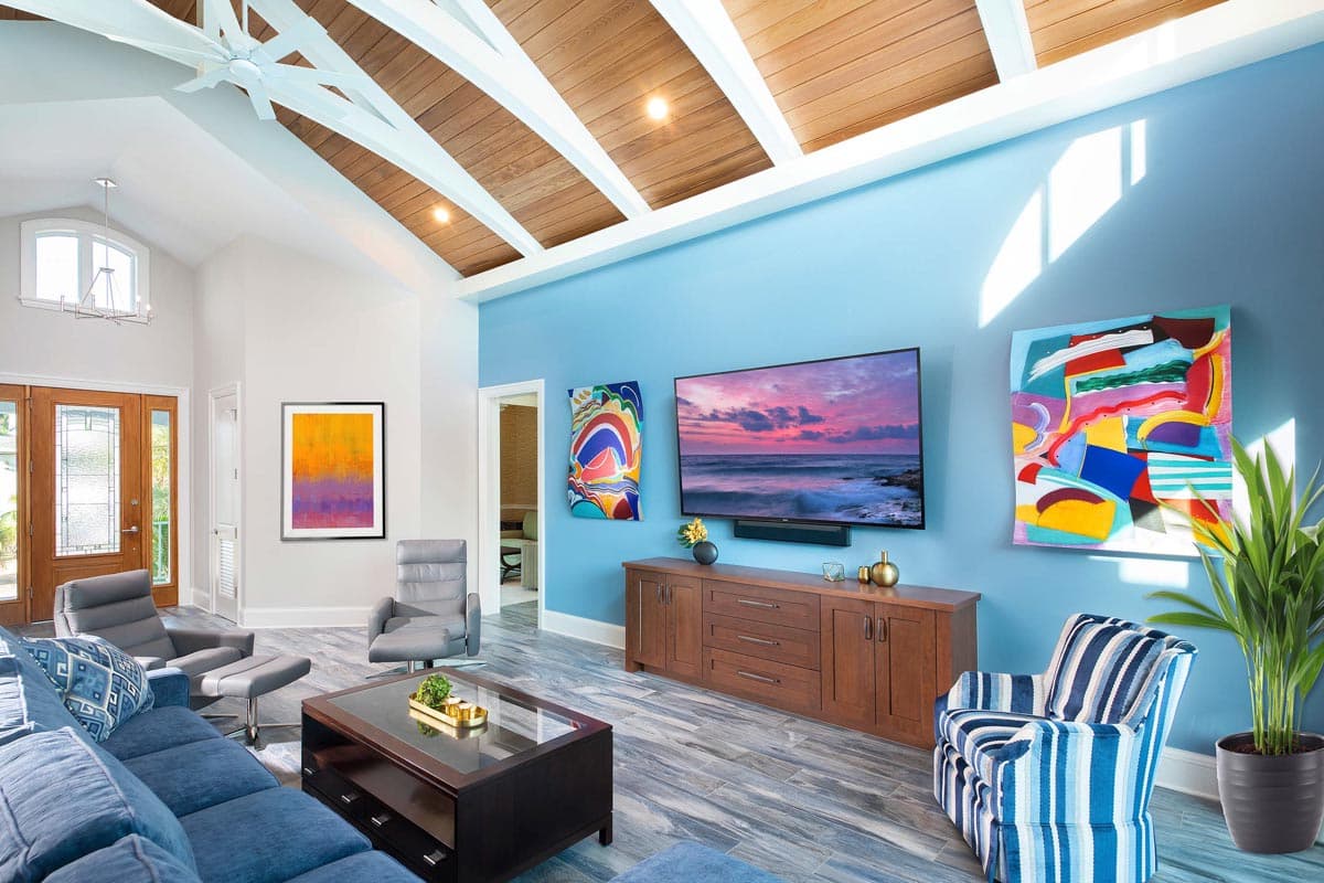 Living room with vaulted wood-paneled ceiling, exposed beams, large windows, and blue accent wall with art.