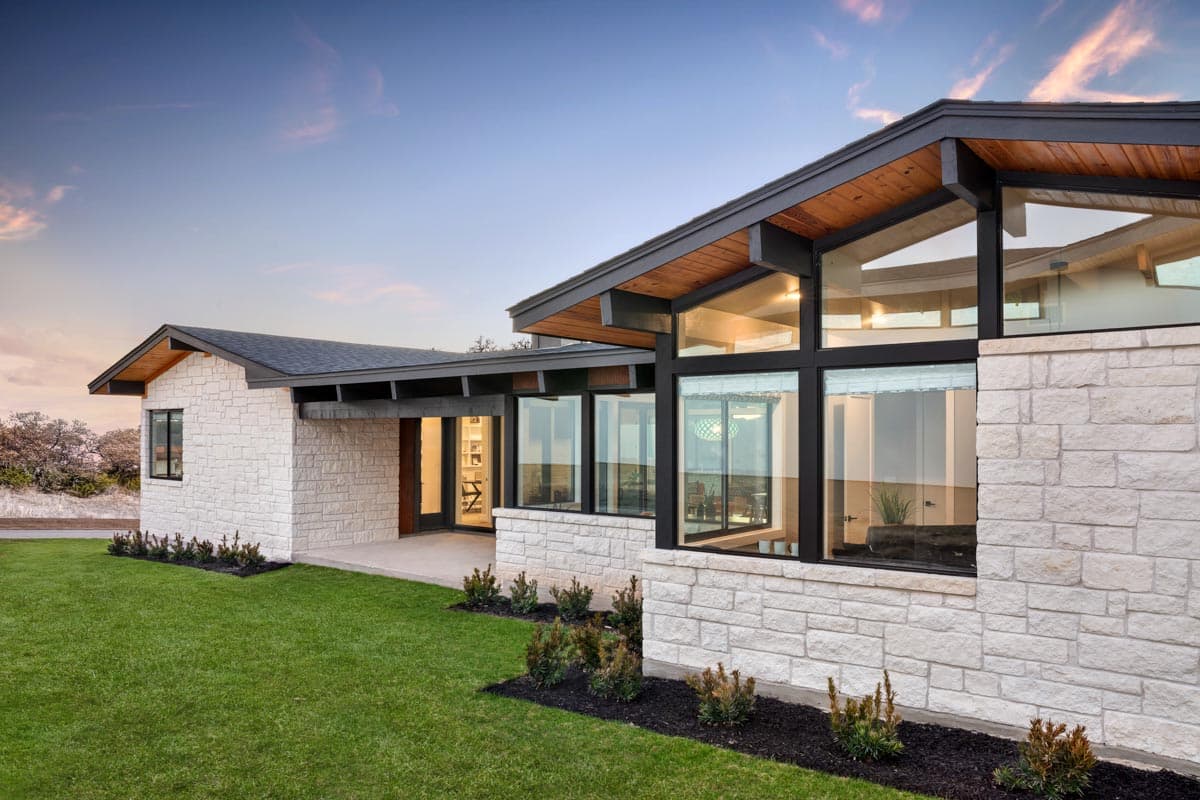 Modern house plan exterior with stacked stone walls, large windows, and a low-pitched roof with exposed wood beams.
