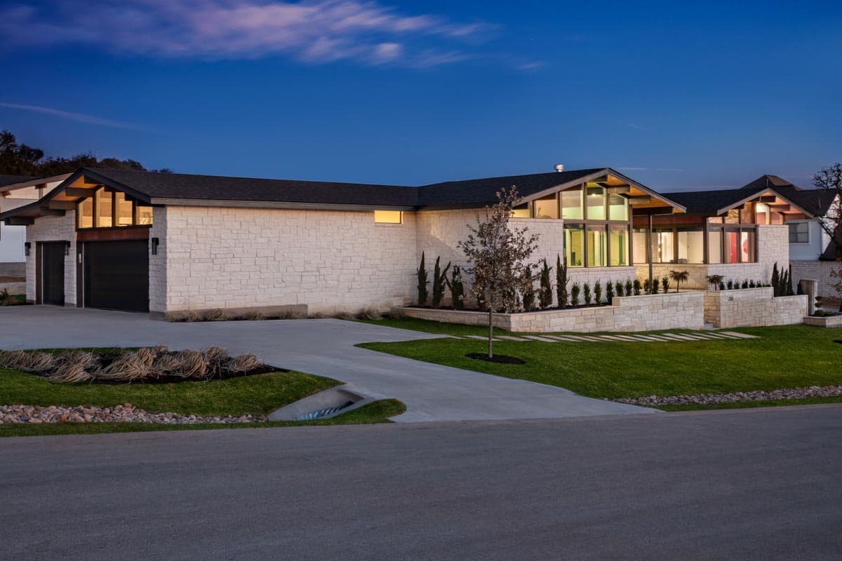 House plan exterior: Modern home with stone facade, gabled rooflines, prominent glass windows, and a two-car garage.