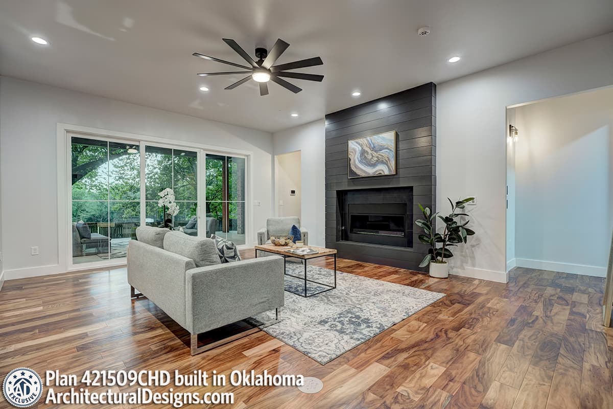 Living room with fireplace, large sliding glass doors, ceiling fan, and wood flooring.