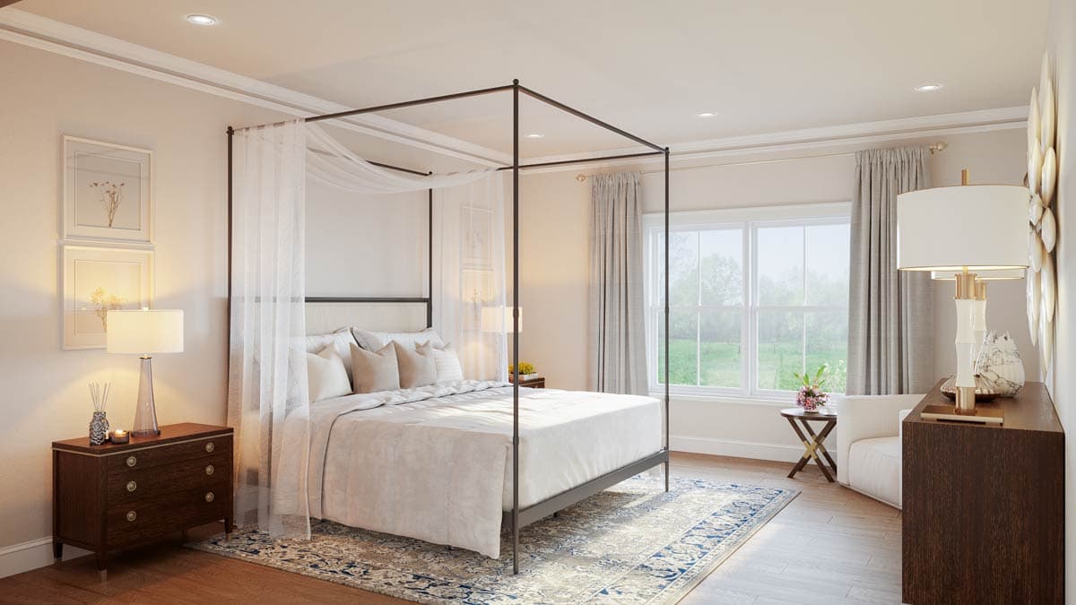 A luxurious bedroom with a four-poster bed draped with sheer curtains. Two framed pictures and a lamp sit on a wooden nightstand.