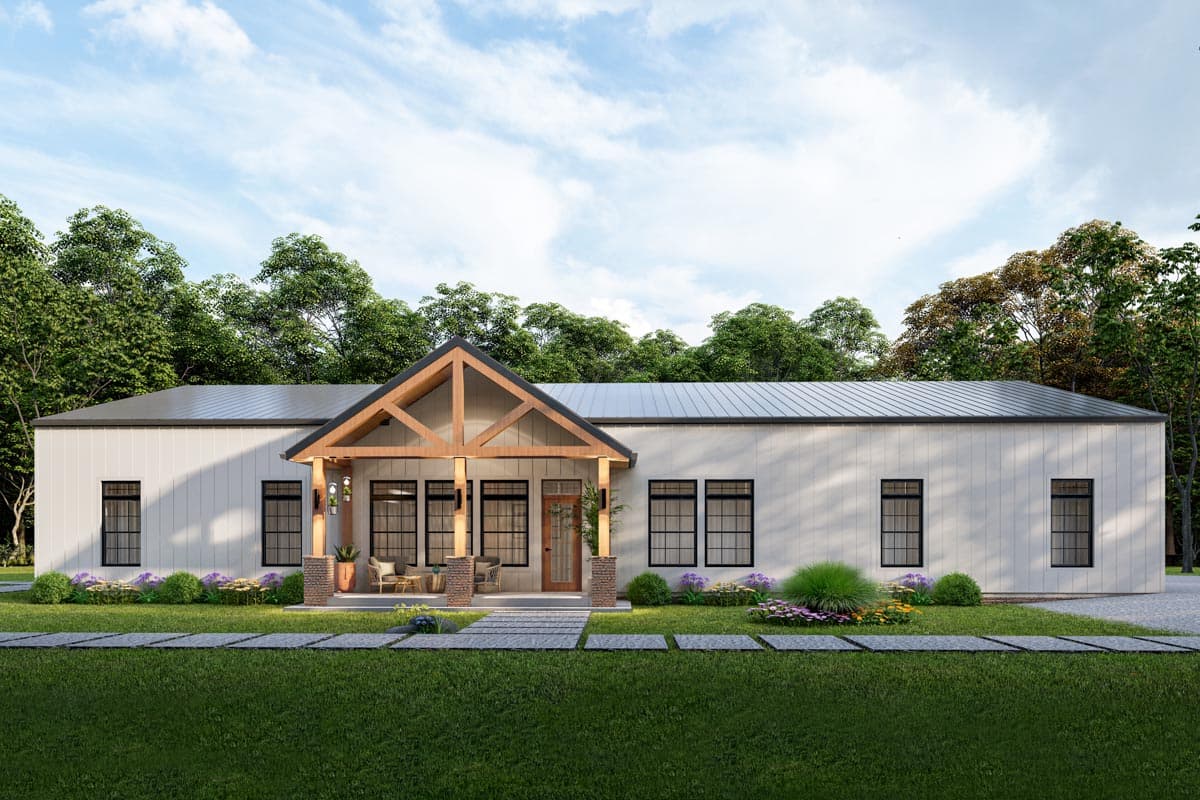Modern, single-story house with a prominent porch and exposed wood beams. A pathway leads to the front door, surrounded by lush green lawn and trees.