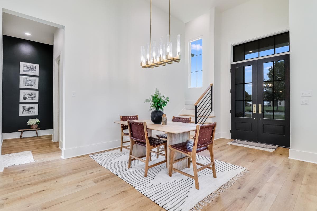 Interior view of dining area with double entry doors, stairs, and tall window.