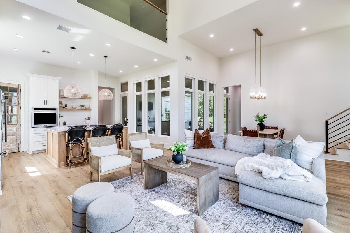 Open concept living area with vaulted ceilings, kitchen island, large windows, and a modern staircase.