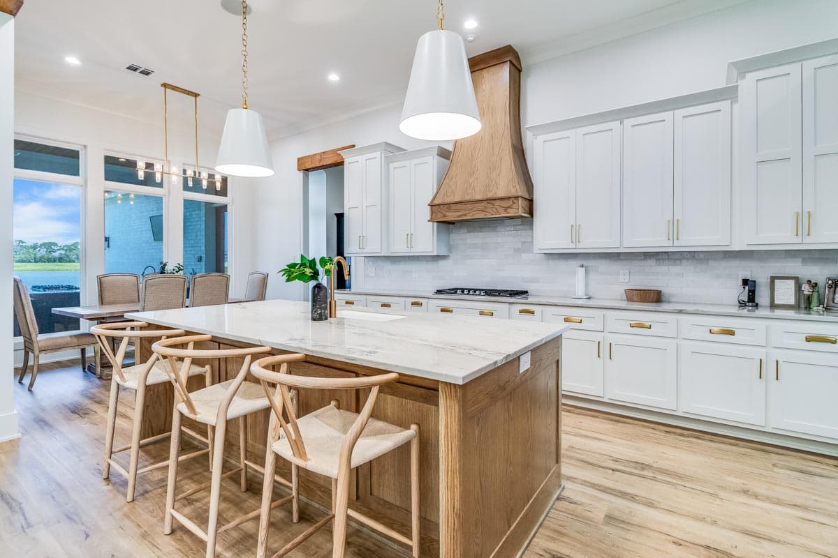 Kitchen interior featuring a large island with seating, a range hood, white cabinetry, and a dining area visible in the background.