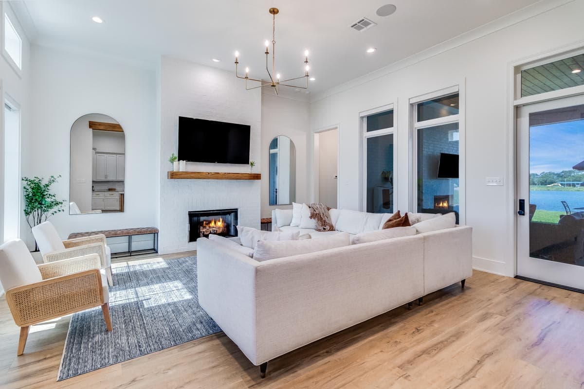 Great room interior with a brick fireplace, built-in television, and an open layout. Includes large windows and a sectional sofa.