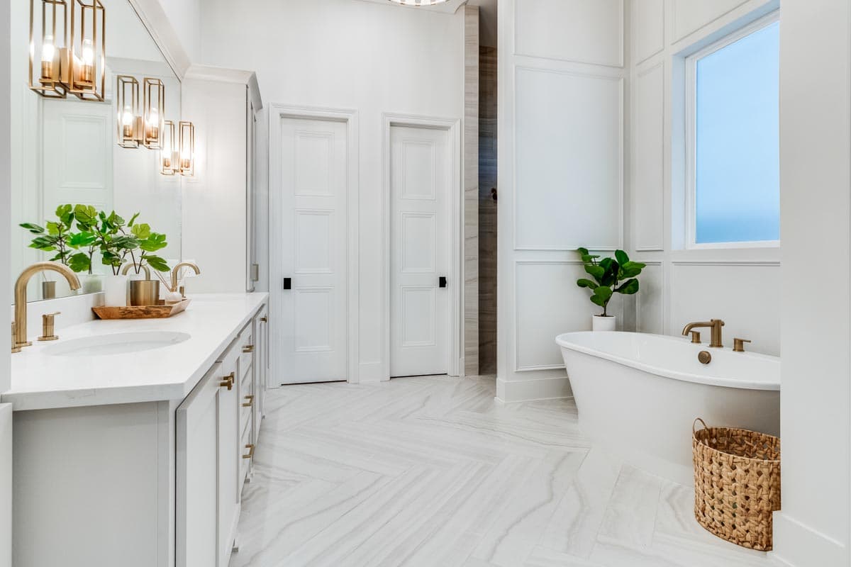 Bathroom interior with freestanding tub, gold fixtures, and herringbone-patterned floor tile. Includes a double vanity with a large mirror.