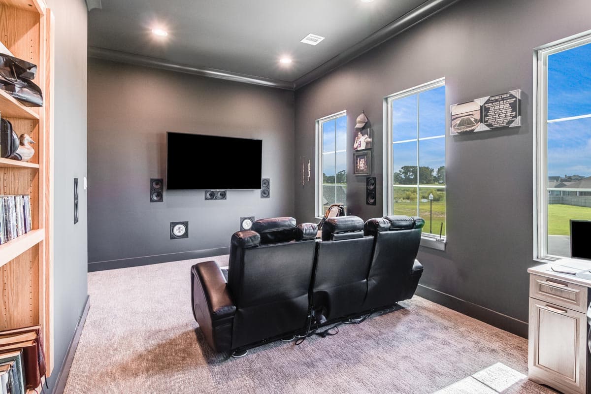 Home theater with a large screen, black leather recliners, and built-in speakers. Features include recessed lighting and windows with exterior views.