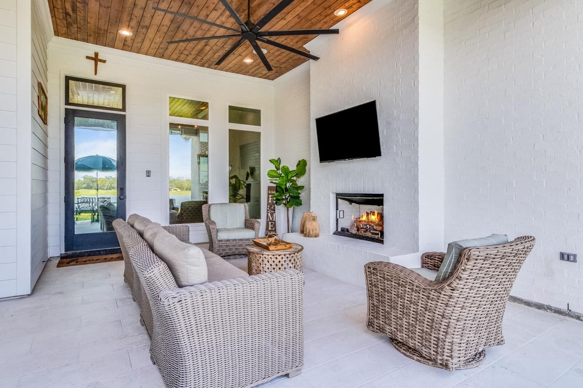 House plan outdoor living area with a fireplace, wicker furniture, and a wood-plank ceiling with a large fan.