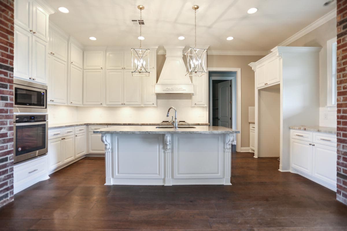 Kitchen with white cabinetry, island with sink, range hood, and dark wood floors.