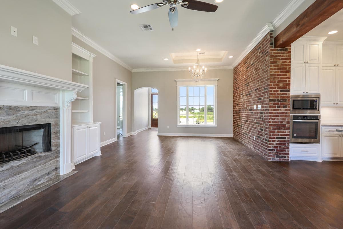 Great room with fireplace, exposed brick wall, and kitchen with white cabinets and stainless steel appliances.