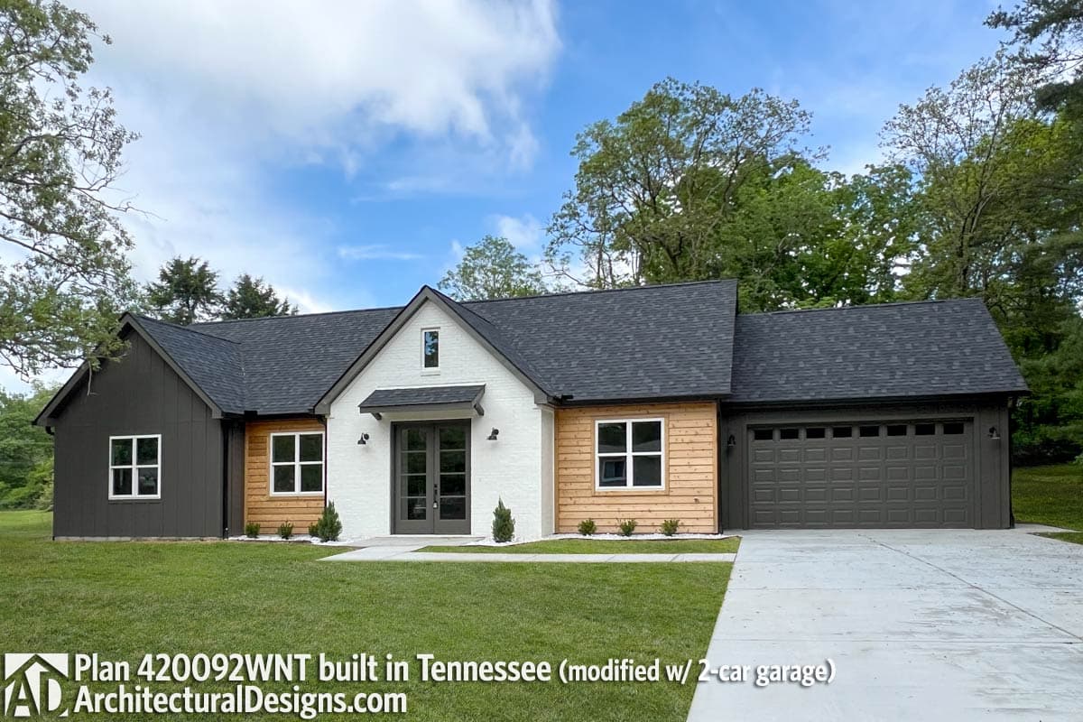 House plan exterior: Modern Farmhouse style, one story, white brick and wood siding, gable rooflines, dormer, and 2-car garage.